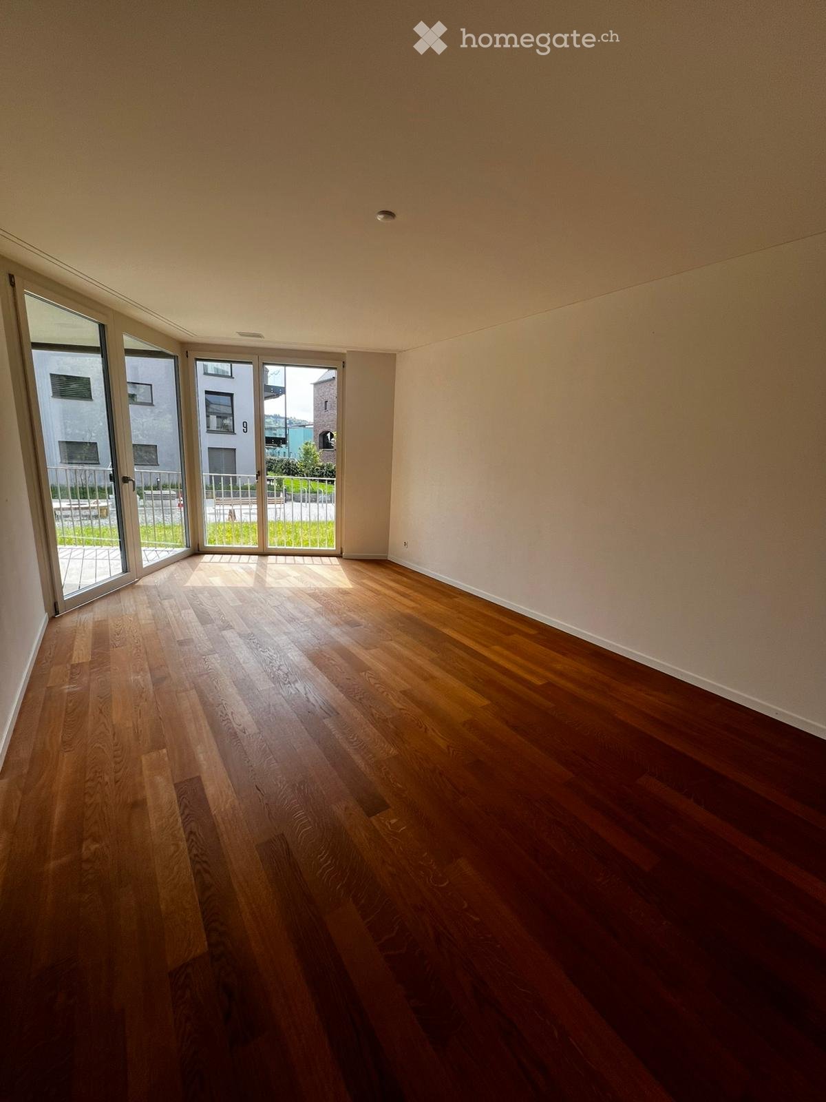 Empty room with hardwood floors, white walls, and large glass doors leading to a balcony.