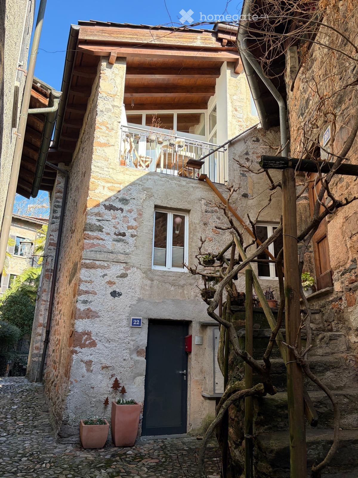 Stone house, wooden balcony, black door, stone wall, two potted plants