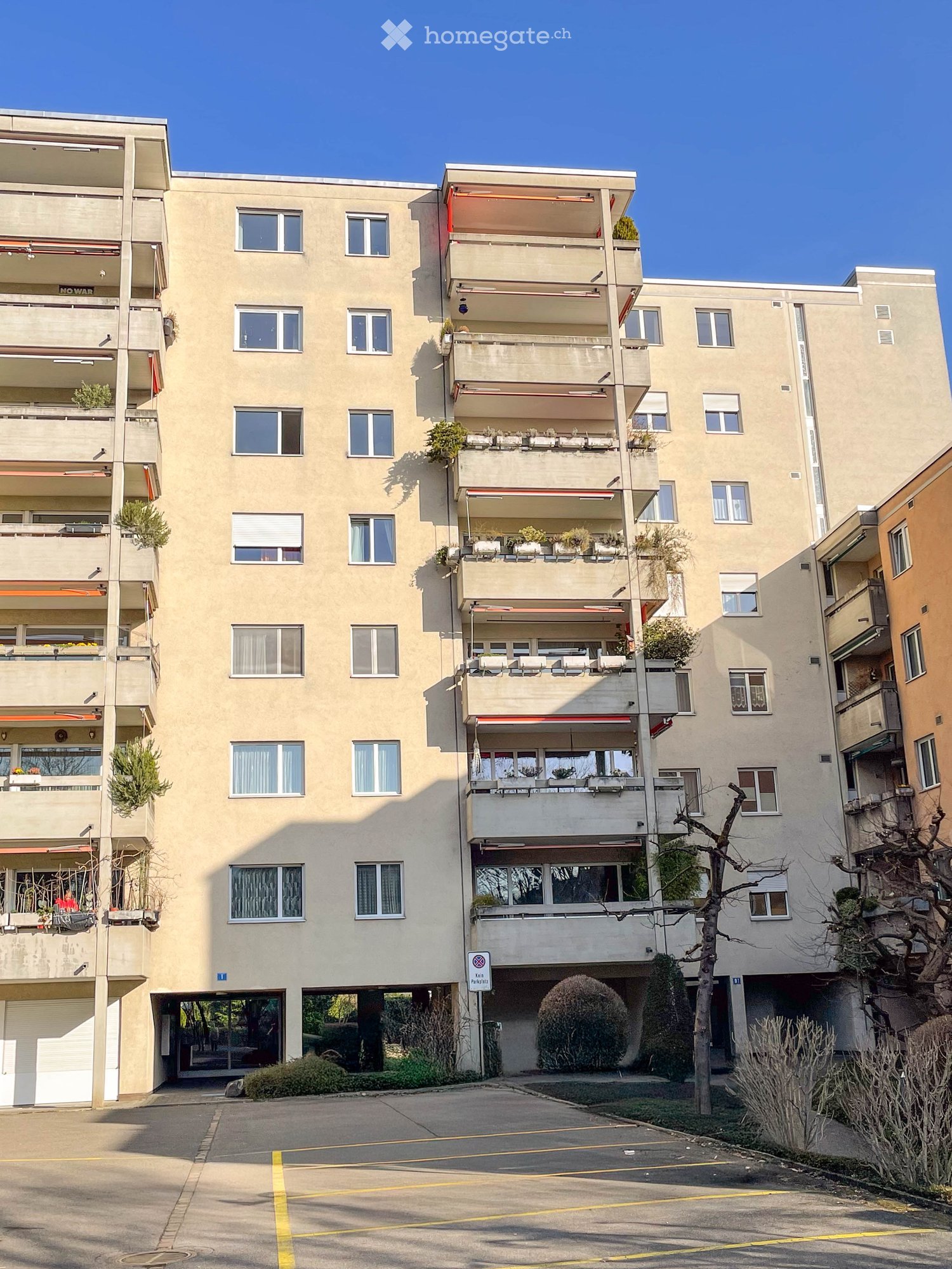 Multi-story building, beige exterior, multiple balconies, parking lot in front