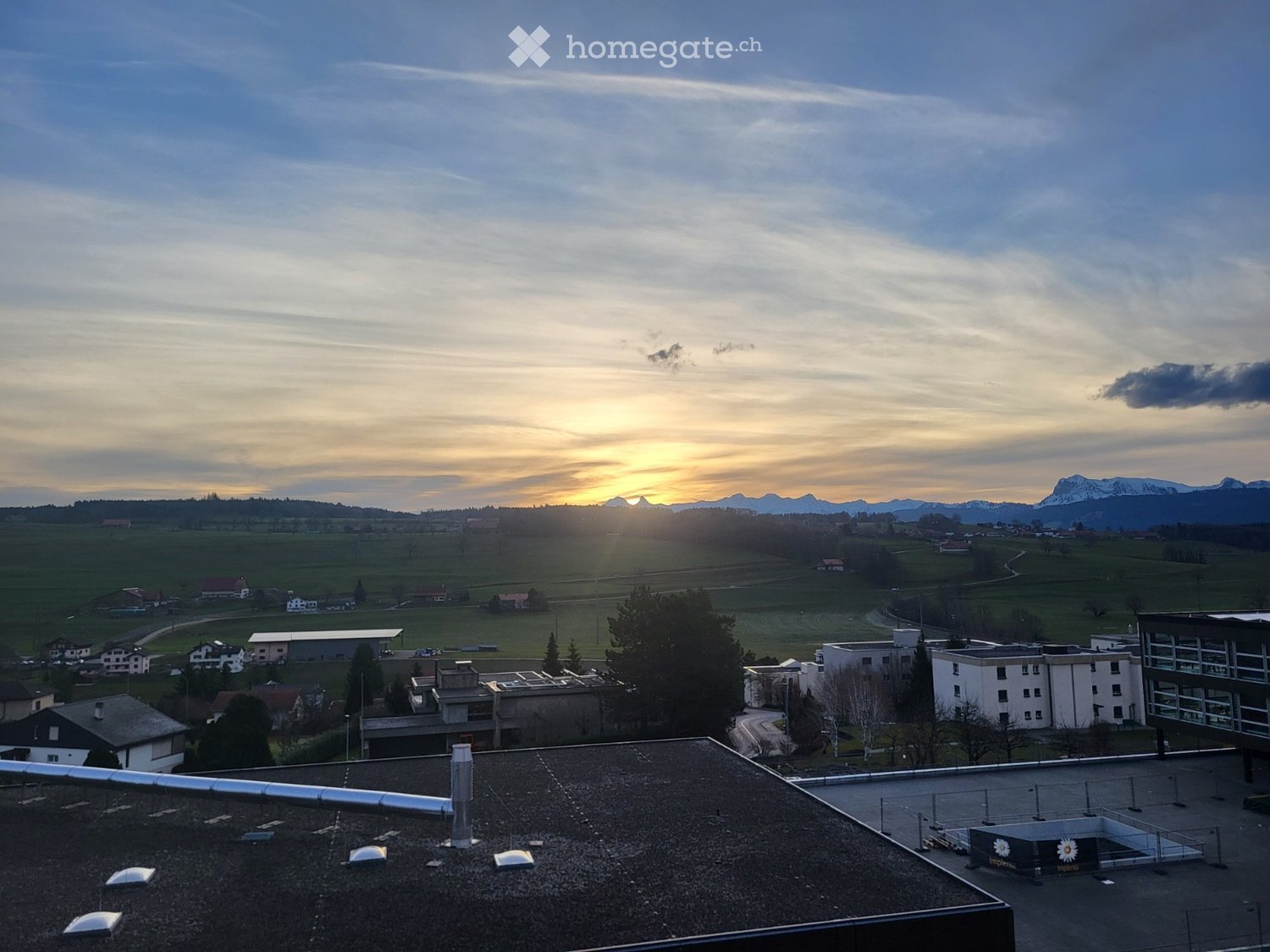 Roof view of a building with surrounding landscape, distant mountains, and sunset sky.