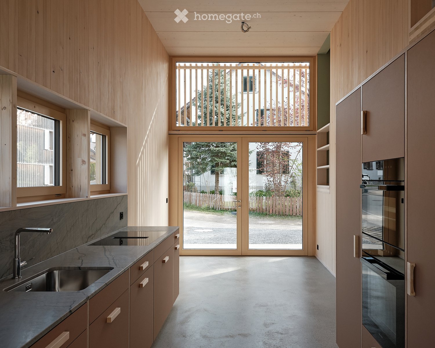 Modern kitchen with wooden cabinets, granite countertops, stainless steel sink, and large windows.