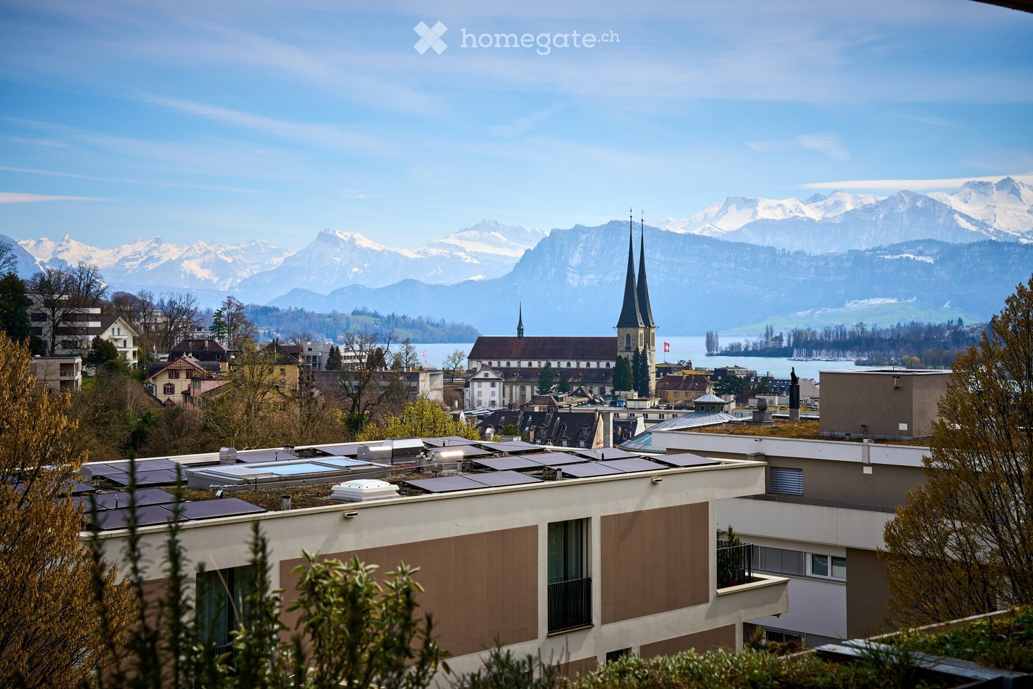 Aerial view of a city with buildings, mountains, and a lake in the background.