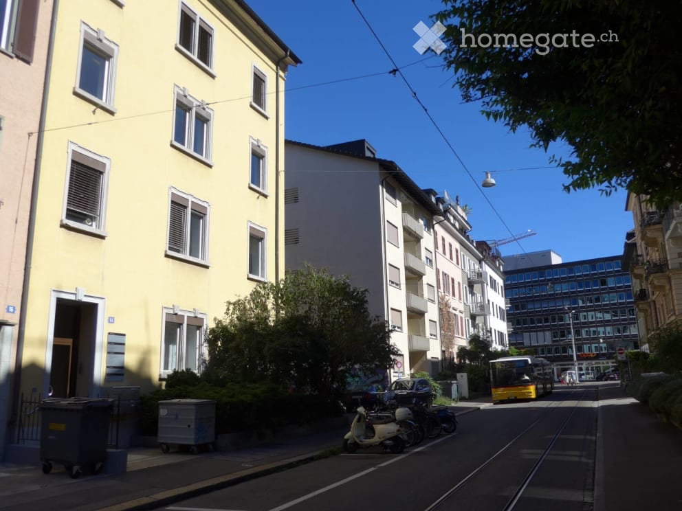 multi-story buildings with numerous windows, street with tram tracks, scooters parked on the sidewalk, and streetlight