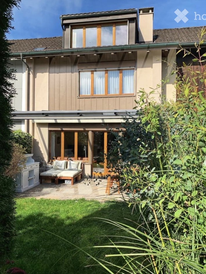{"visible_features": ["Garden / Outdoor Area"], "type": "House", "objects": ["daybed", "cushions", "wooden table", "white cabinet", "faucet"], "description": "Two-story house with wooden exterior, large windows, and a patio with a daybed and cushions.", "