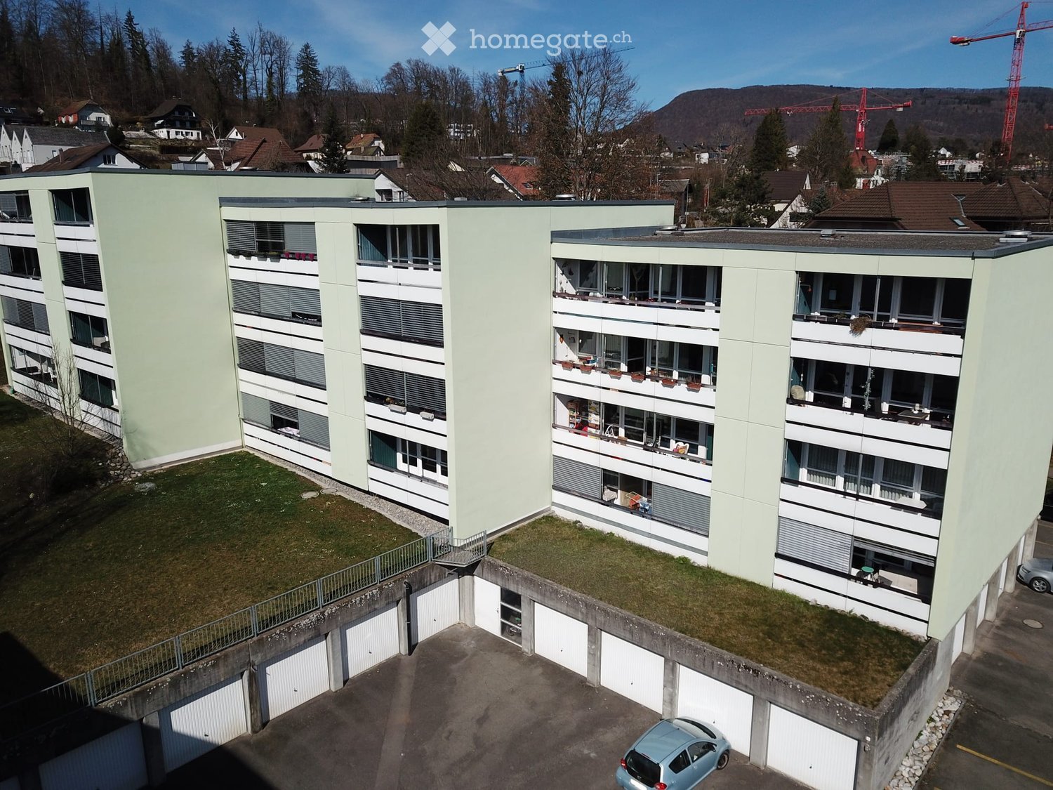 Building. Modern multi-story residential building with light green and white facade, multiple balconies, and surrounding greenery.