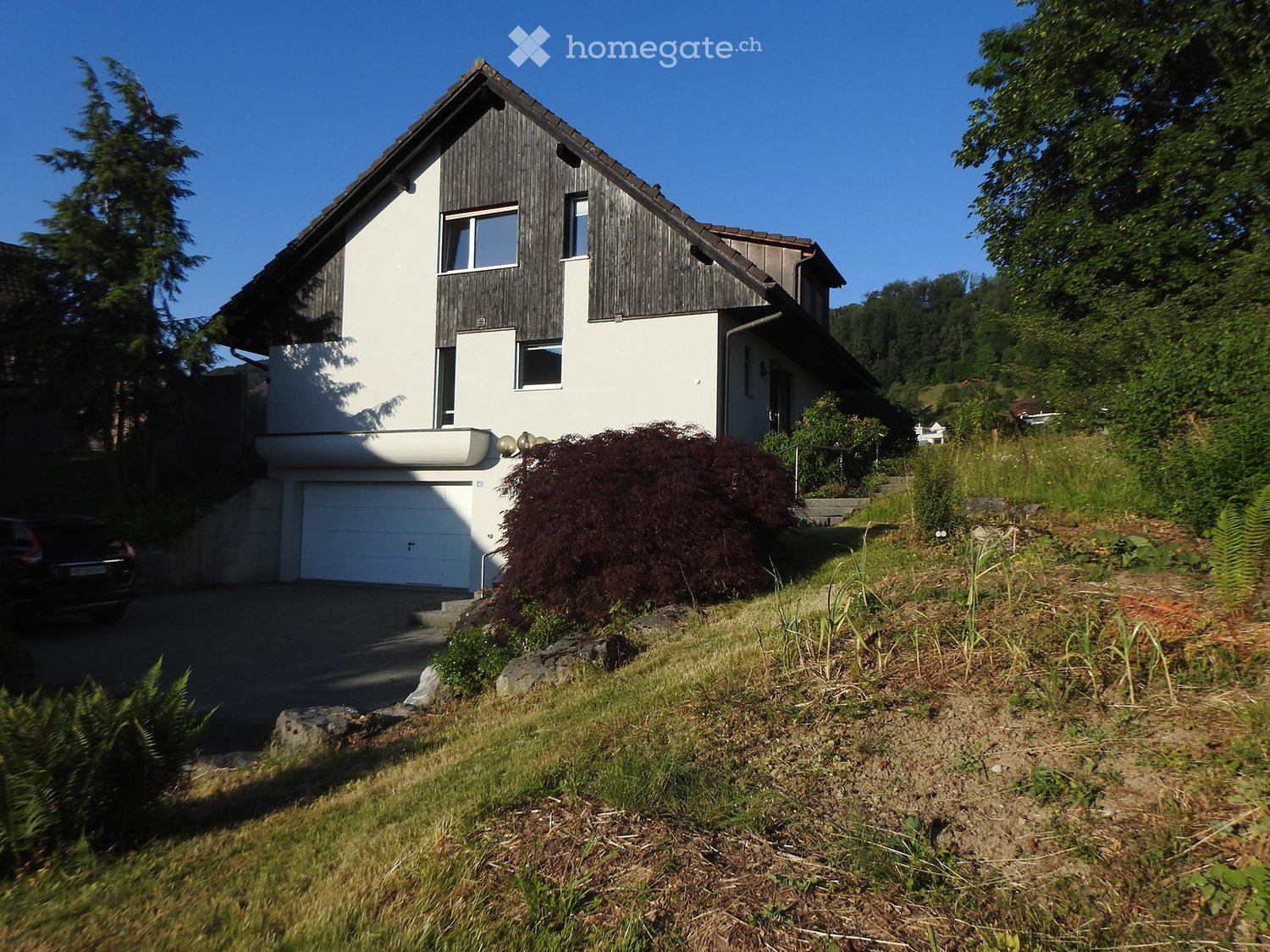 Two-story house with white and dark wood exterior, garage, and surrounding greenery.