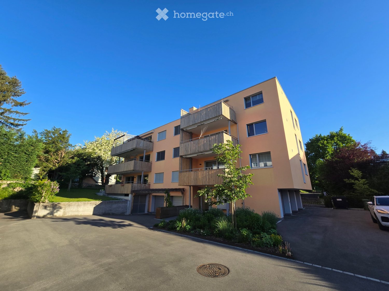 4 story apartment building, beige exterior, balconies, parking lot, trees