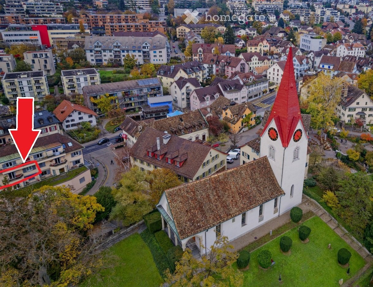 Church with red roof, surrounded by houses, trees, and grass, located in a city