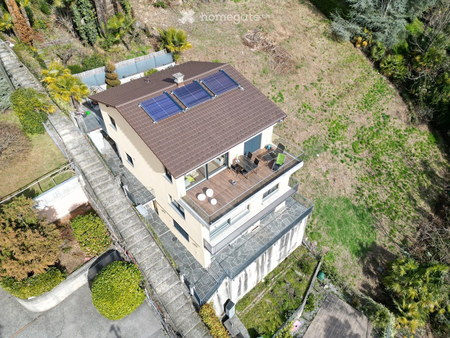 modern house, brown roof, solar panels, terrace with furniture, surrounded by greenery