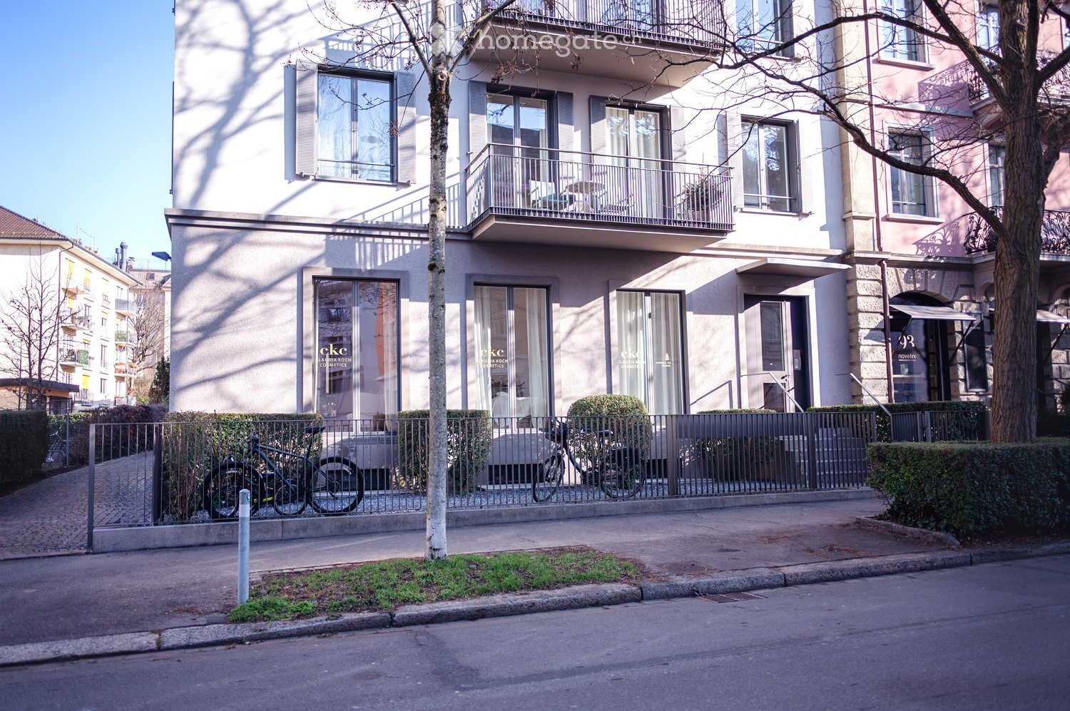 Building. Modern multi-story building with large windows, balconies, and a fenced entrance area with bicycles parked nearby.