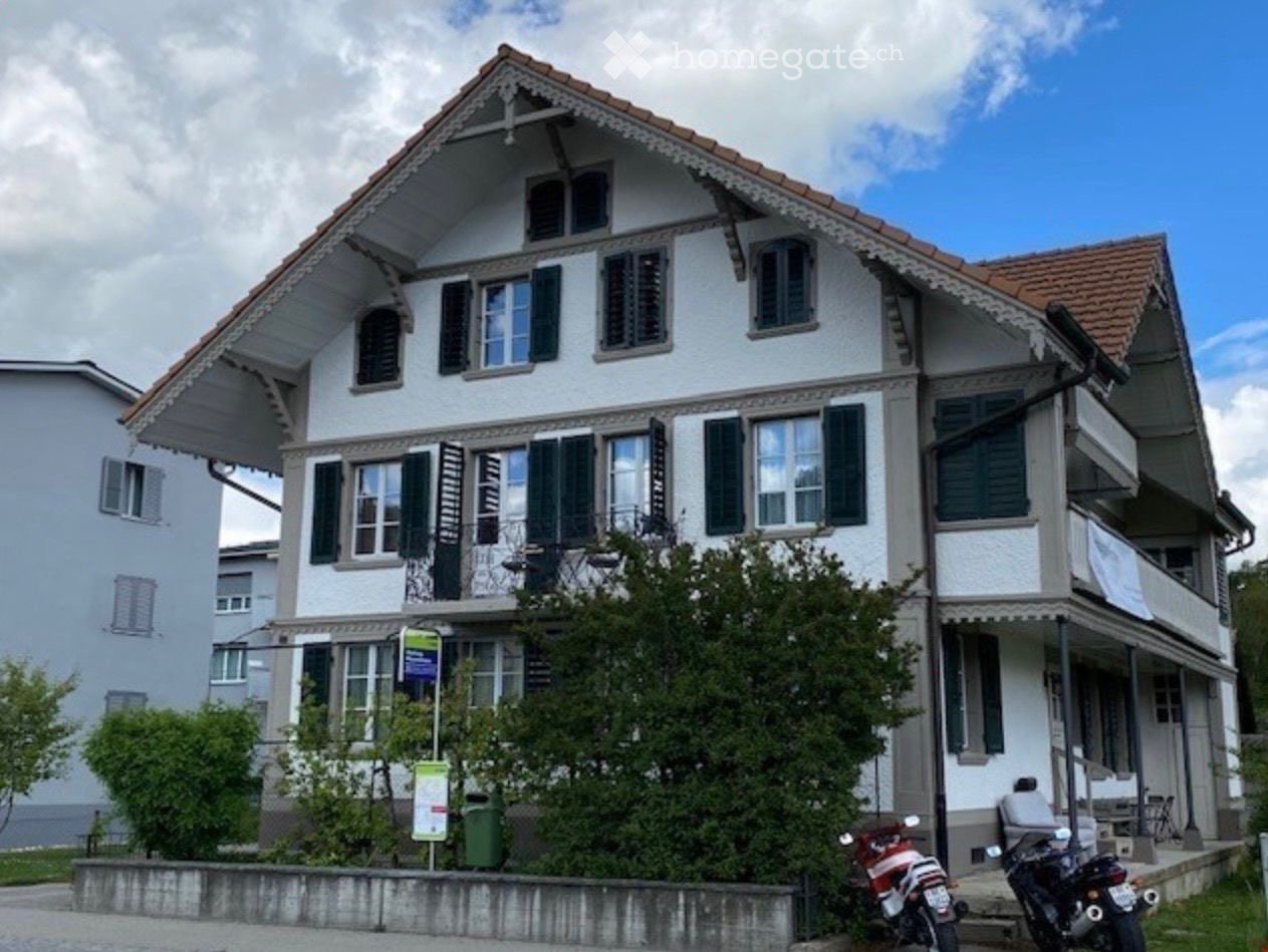 2 story house, white exterior, brown roof, multiple windows, balcony, plants, motorcycles parked