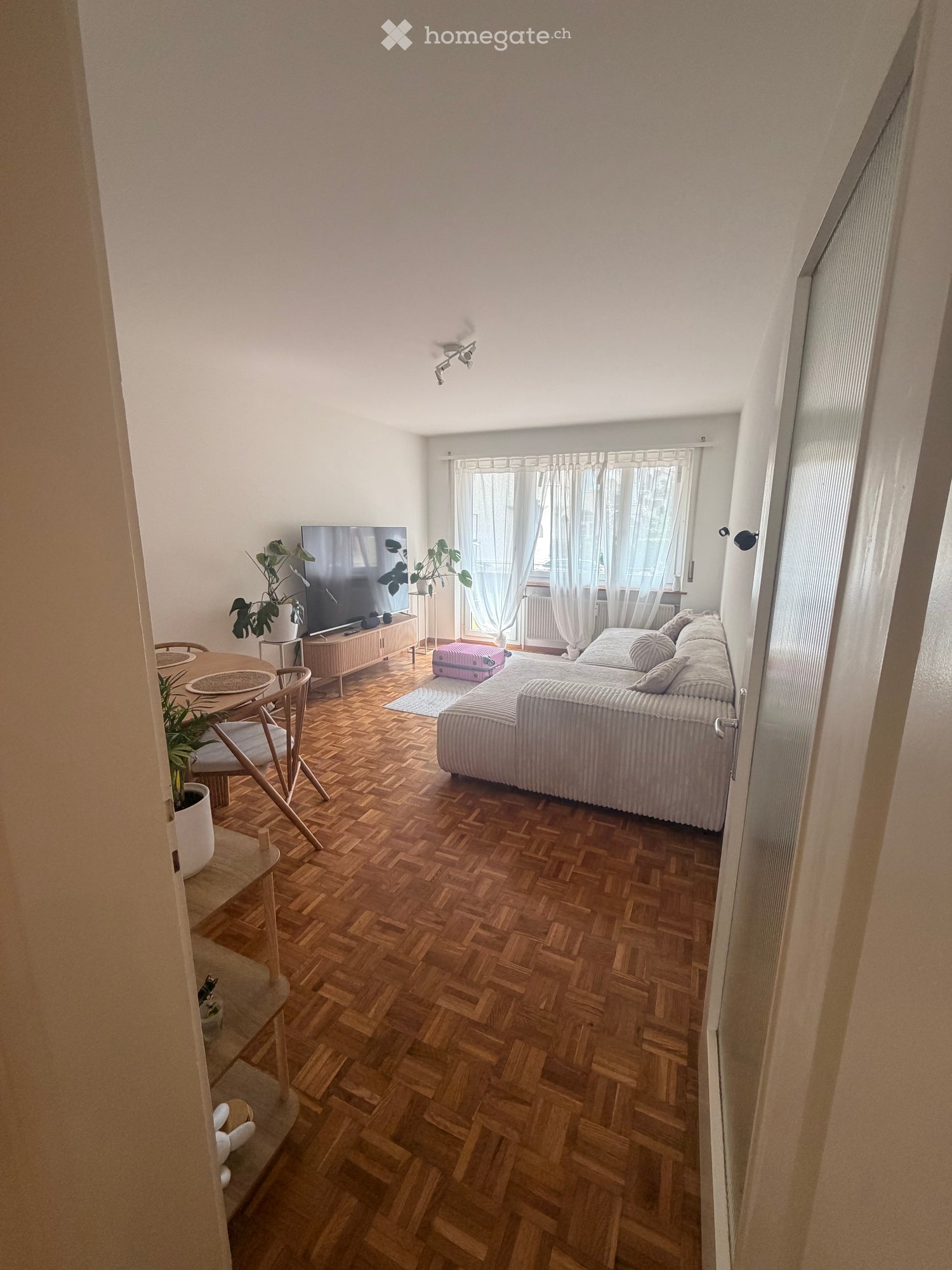 Living Room. Living room with wooden herringbone flooring, a grey sofa, a coffee table, a dining area with a round table and chairs, and a television on a wooden stand.