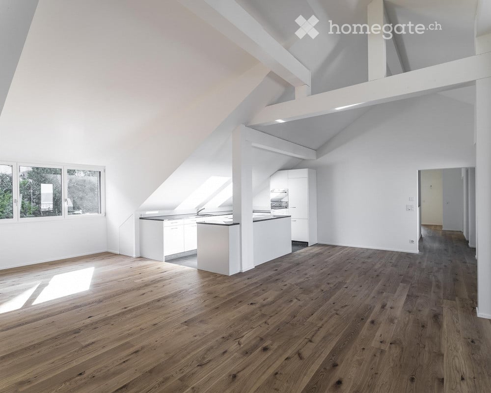 Spacious room with wooden floor, white walls, high ceiling, a kitchen area with cabinets and countertops, and a window.