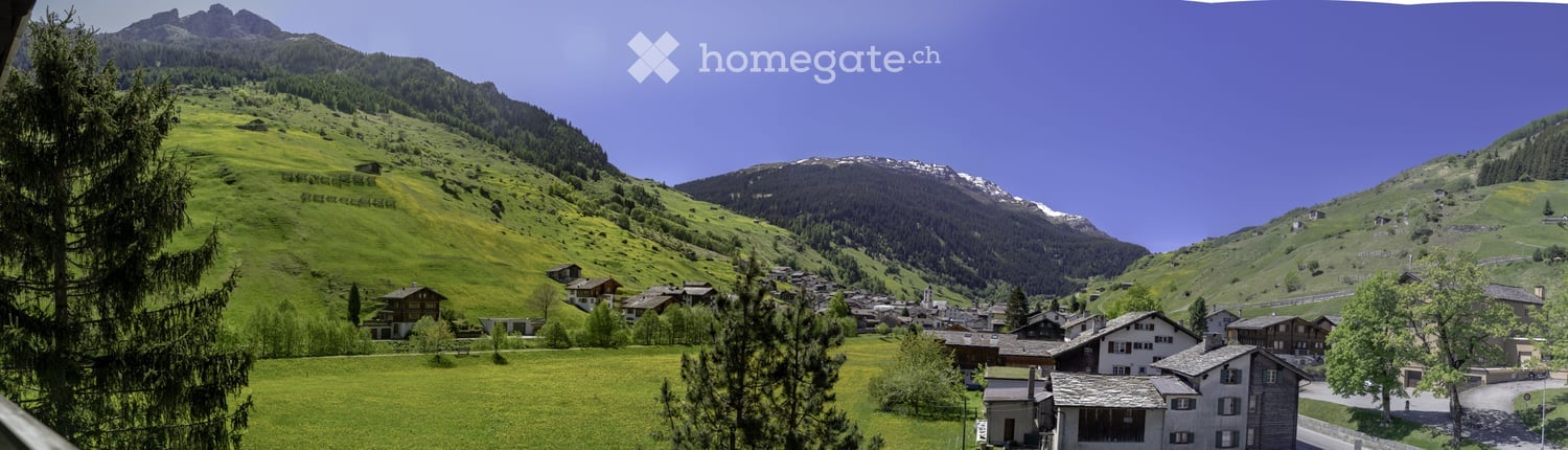 A picturesque alpine village nestled in a lush green valley surrounded by snow-capped mountains. Traditional wooden houses and chalets dot the landscape, with a clear blue sky overhead.