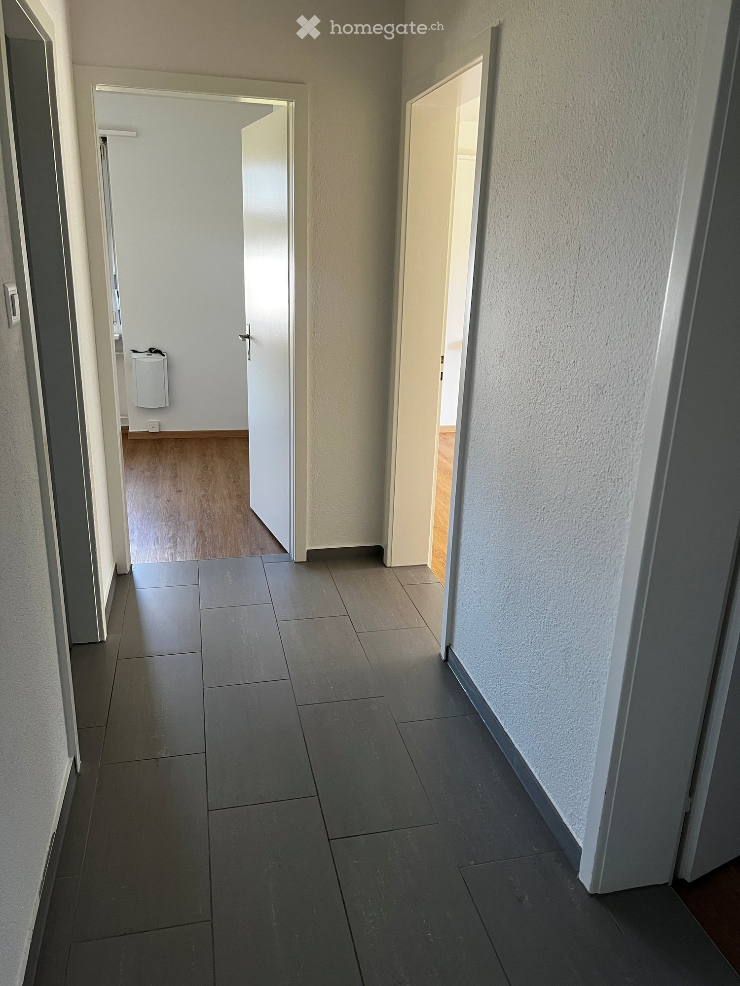 Empty hallway with tiled floor, white walls, wooden floors in rooms, open doors