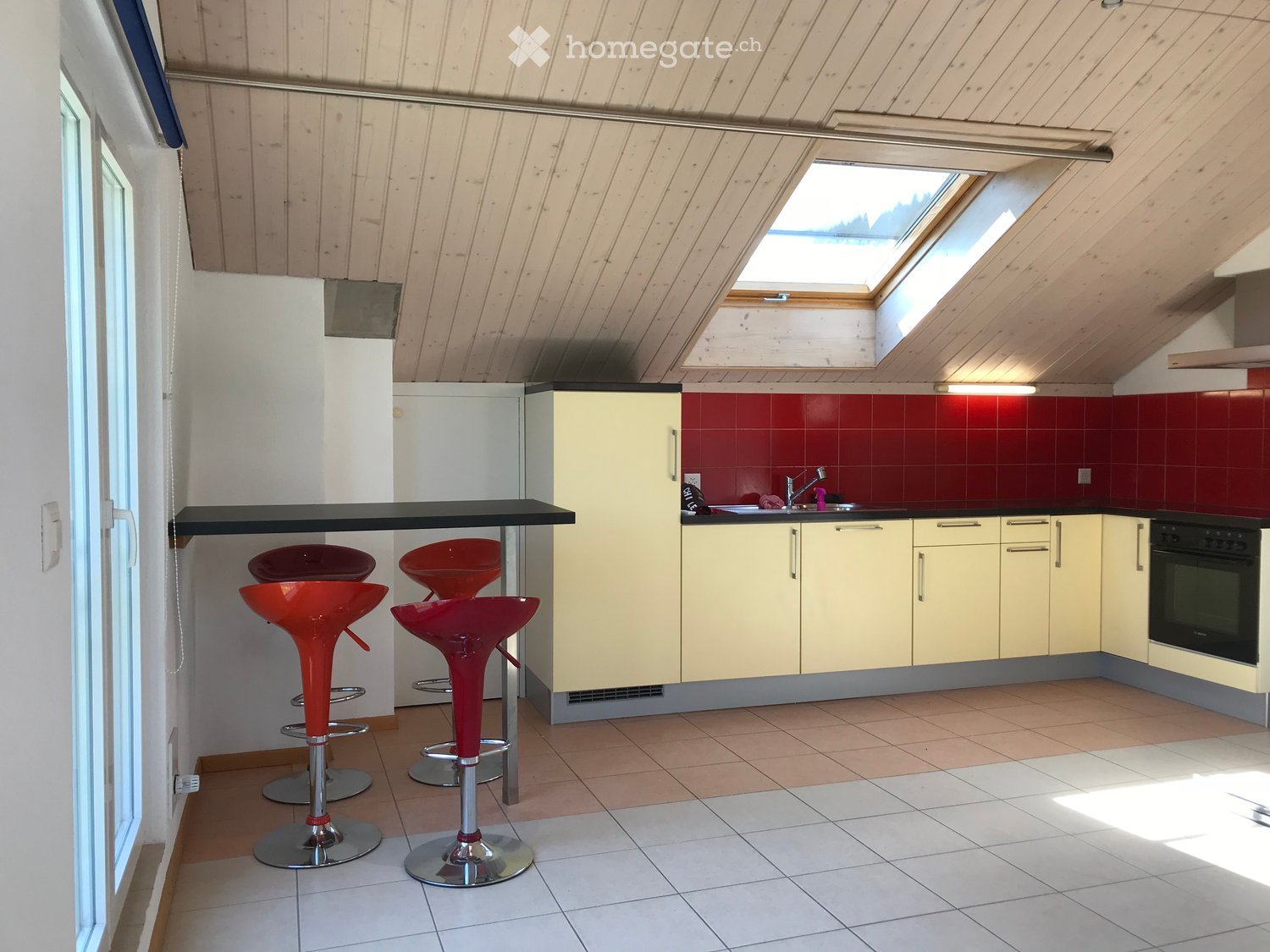 Modern kitchen with red tiled backsplash, light yellow cabinets, black countertop, and four red bar stools.