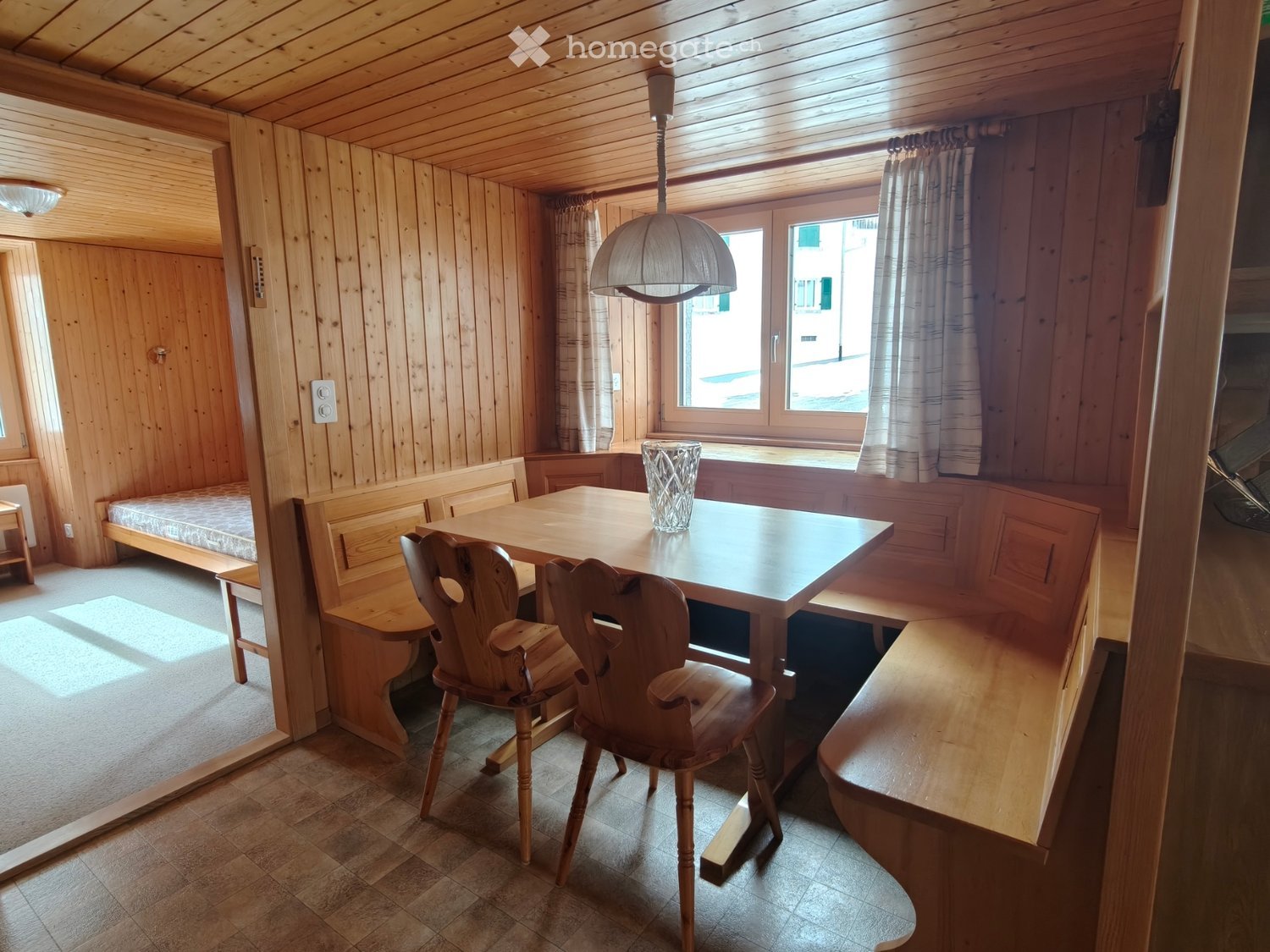 small dining area, wooden table, wooden chairs, wooden bench, ceiling lamp, window with curtain