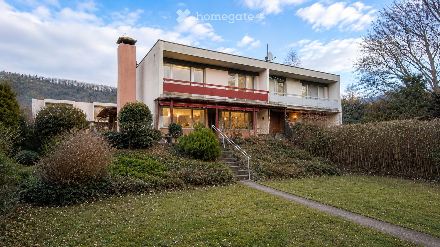 Building. Modern two-story building with a red balcony, surrounded by greenery and a grassy lawn.