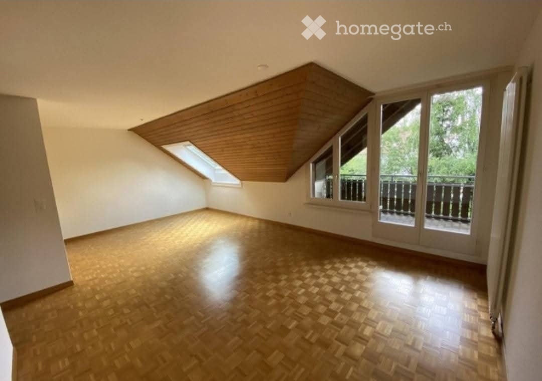 Empty attic room with wooden floor, skylight windows, and sliding glass doors leading to a balcony.
