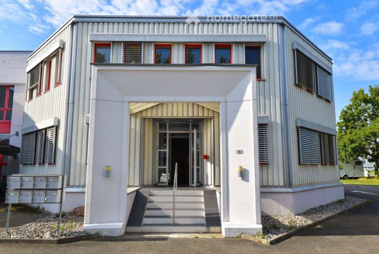 Building. Modern, single-story building with a white facade, red-framed windows, and a central entrance with steps and a small canopy.