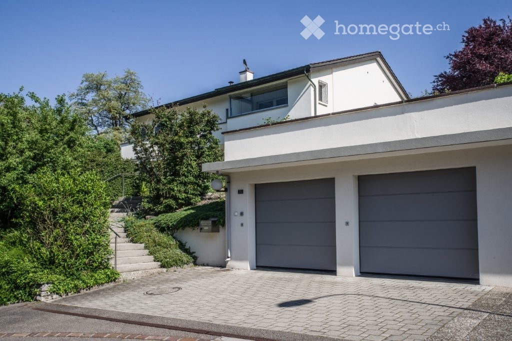 A white house with a two-car garage on a sloped driveway with a white tiled pathway.