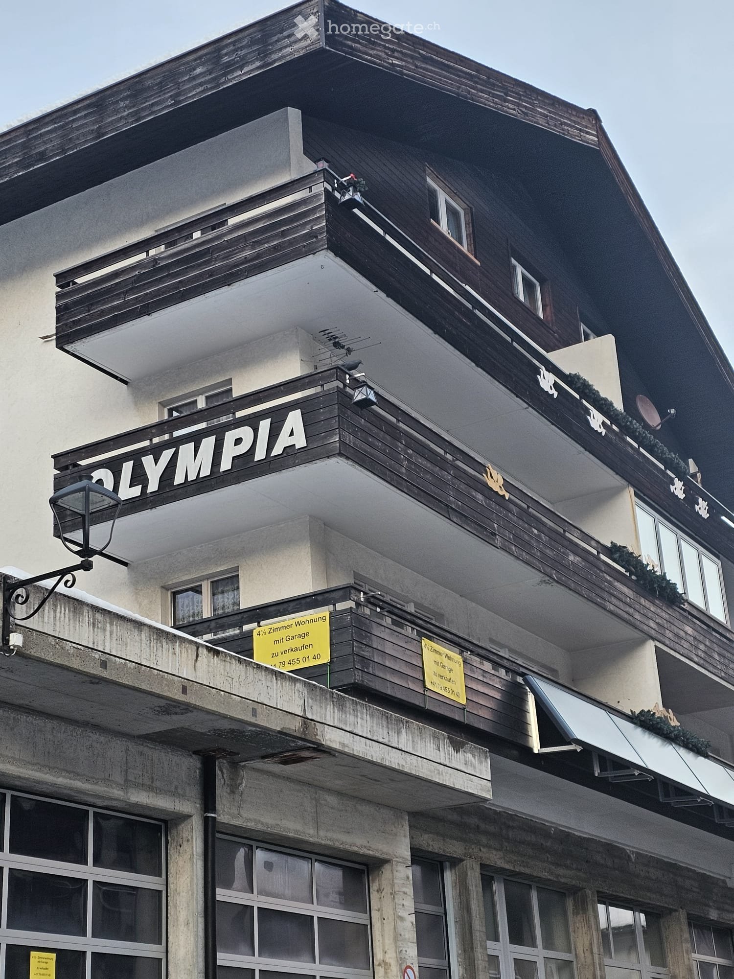 3 story building, wooden balconies, yellow sign reading 'OLYMPIA', glass windows, concrete base