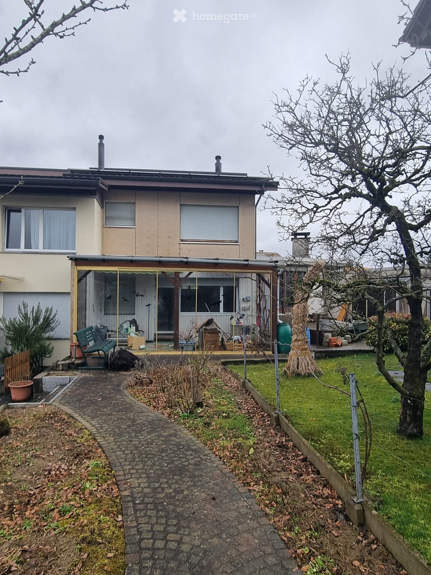 Garden / Outdoor Area. Garden area with a paved pathway leading to a covered patio, featuring a bench, potted plants, and a grassy lawn.