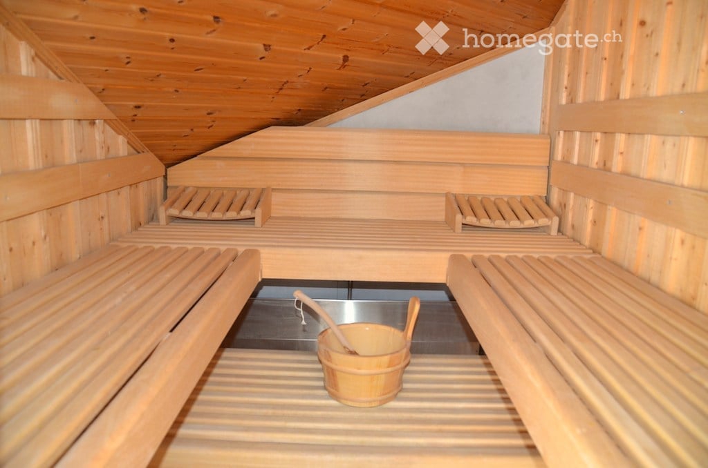 Wooden sauna with multiple benches, a small wooden bucket, and a wooden spoon placed on the floor.
