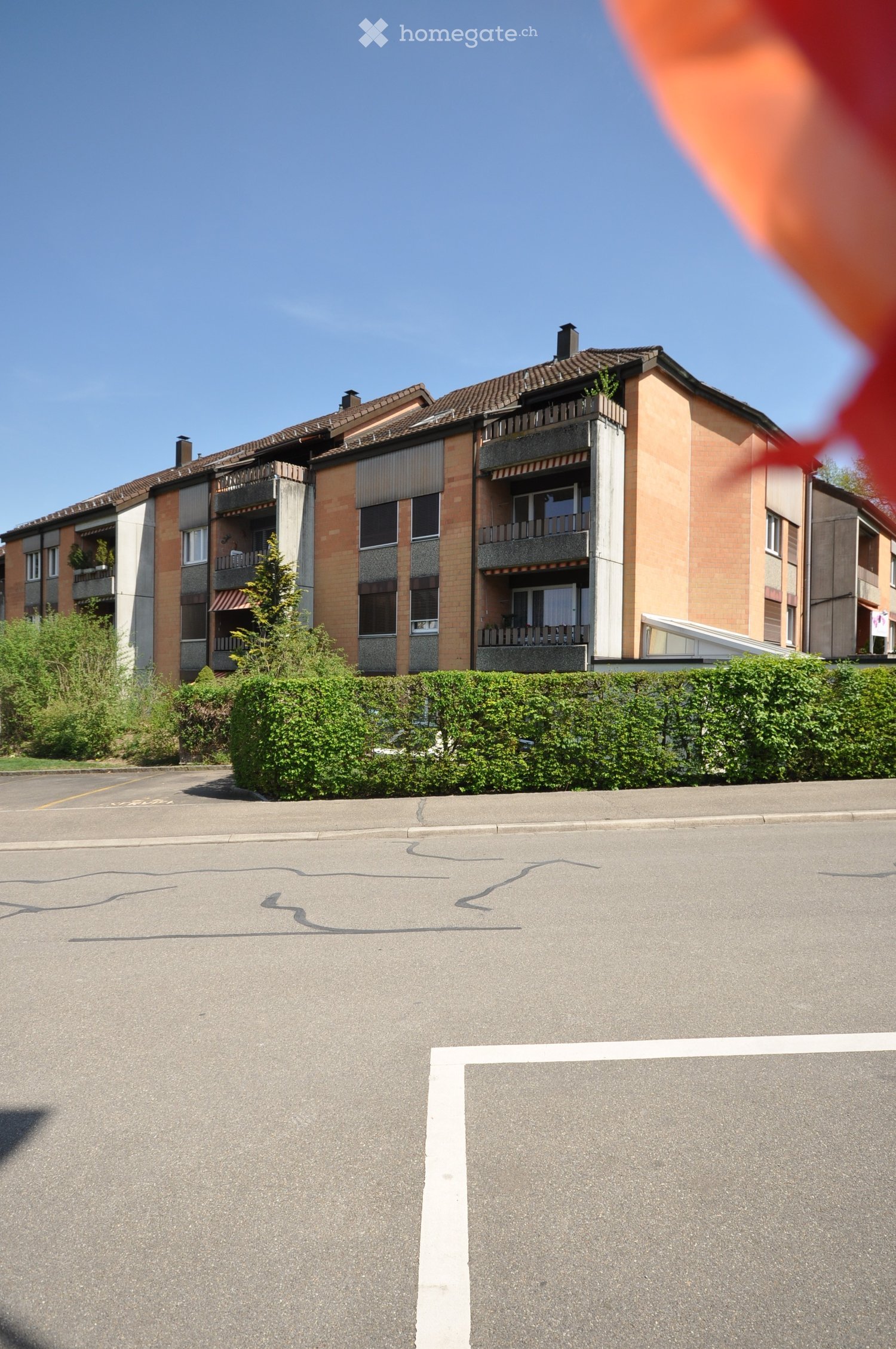 Building. Multi-story apartment building with balconies, surrounded by greenery and a parking area.