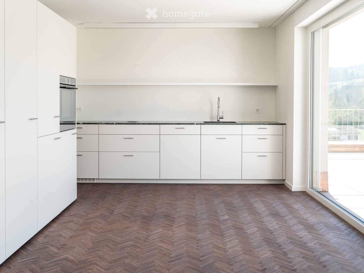 Kitchen. Modern kitchen with white cabinets, dark countertops, and herringbone wooden flooring. Features an integrated oven and a sleek faucet.