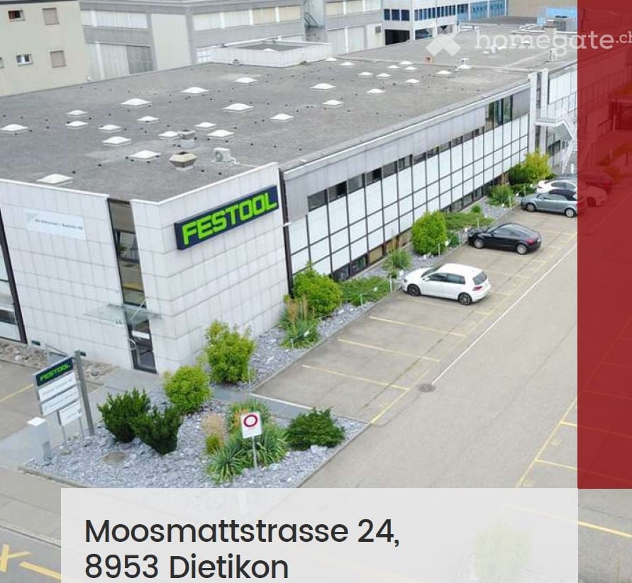 Building. A modern industrial building with a flat roof, large windows, and a parking lot with several cars. The building has a sign reading "FESTOOL" on its facade.