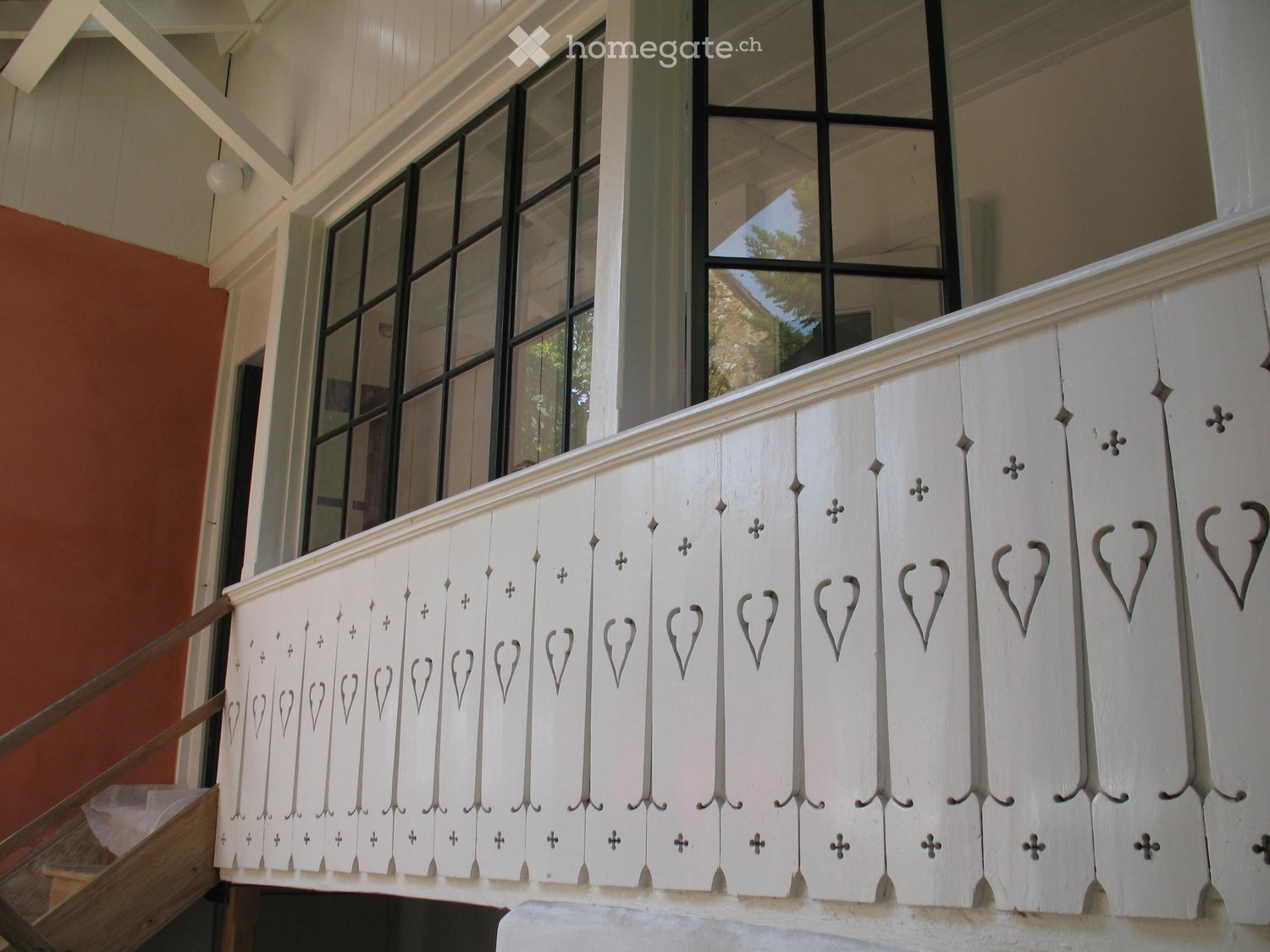 Balcony / Terrace. White wooden balcony railing with decorative heart and cross patterns, large windows in the background.