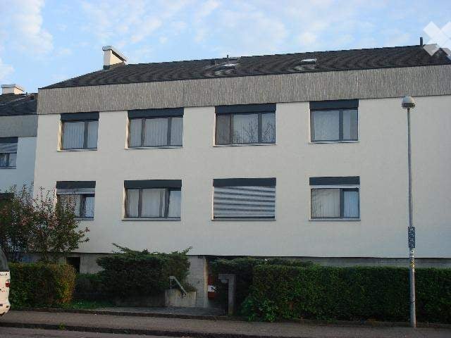 Building. A modern multi-story residential building with white exterior walls, multiple windows with blinds, and a flat roof.
