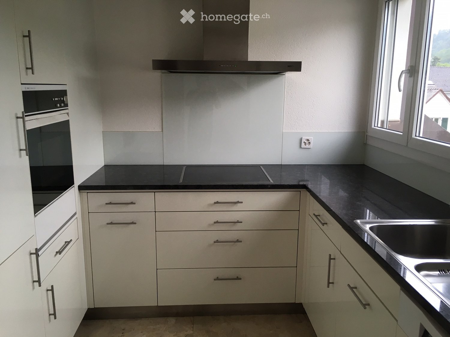 Kitchen. Modern kitchen with white cabinets, black countertops, stainless steel sink, built-in oven, and range hood.