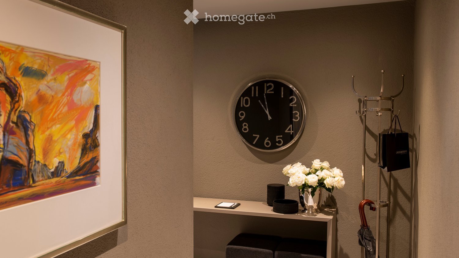 Furnished Room. A modern hallway or entryway with a sleek white console table, a vase of white flowers, a clock, and a coat rack with an umbrella and a handbag.