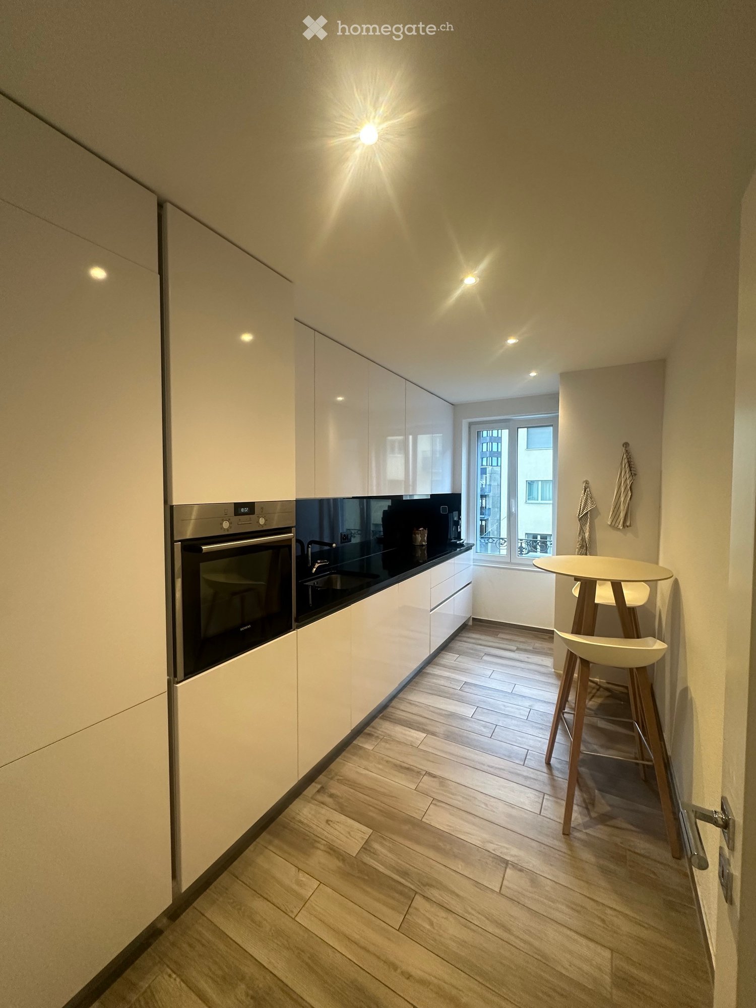 modern kitchen with white cabinets, black countertops, wooden floor, built-in oven, sink, window with city view