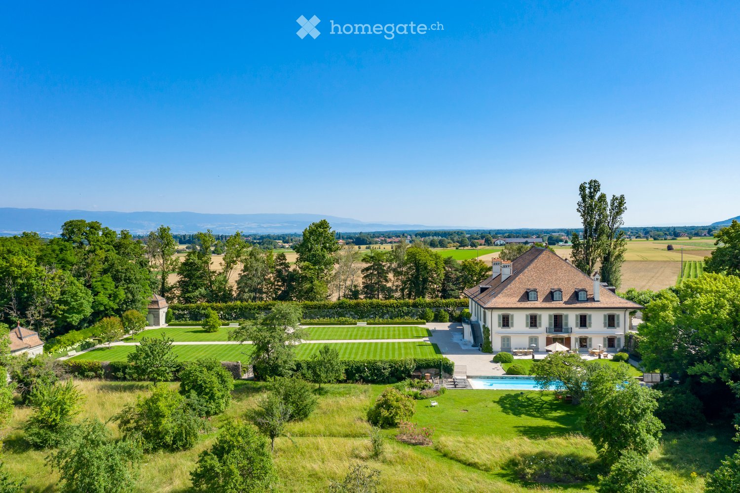 House. Luxurious country house, surrounded by vast lawns, multiple trees, swimming pool, mountain range in background