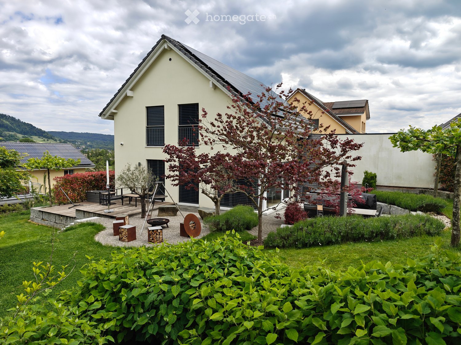 Garden / Outdoor Area. Well-maintained garden with a modern house in the background, featuring a patio, seating area, trees, shrubs, and a fire pit.
