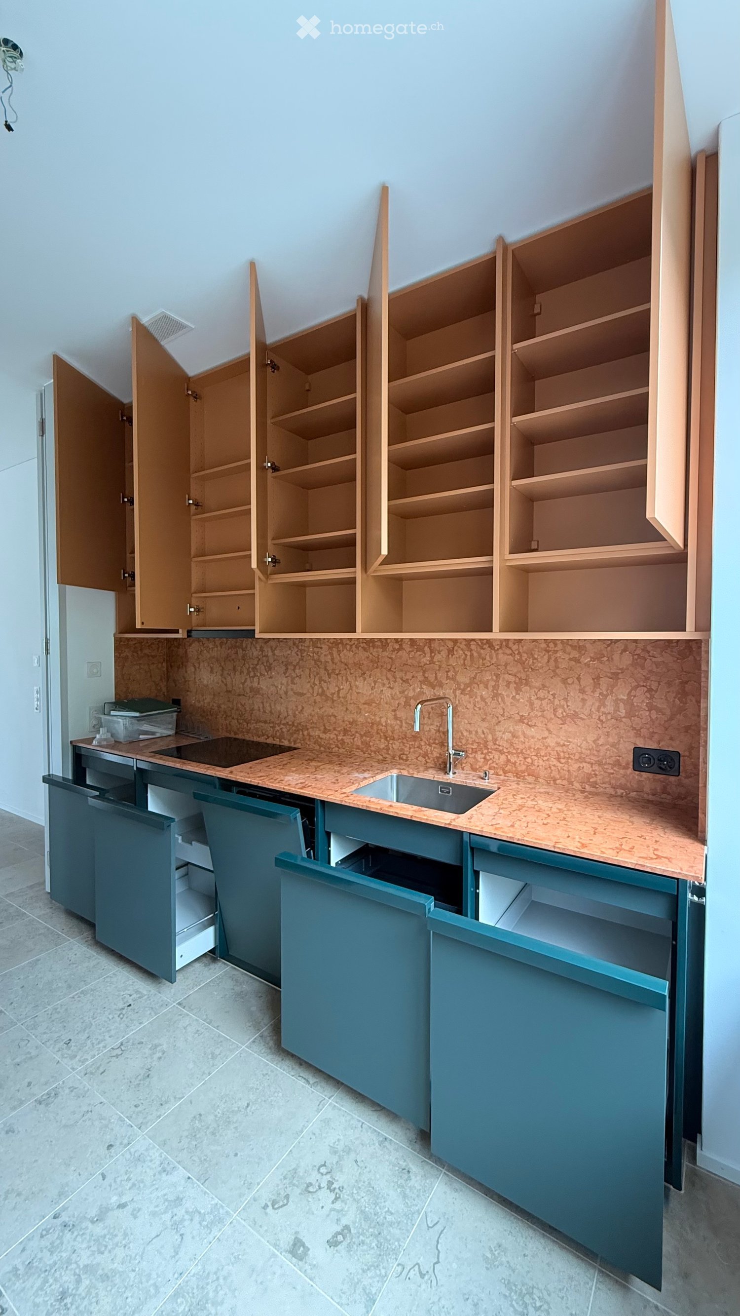 Kitchen. Modern kitchen with light wood cabinets, teal lower cabinets, and a copper-toned countertop. The sink and faucet are visible, and the cabinets are open, revealing empty shelves.