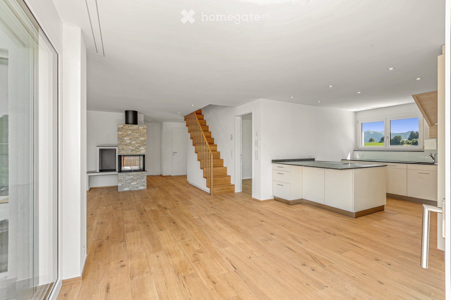 Furnished Room. Open-plan living and kitchen area with wooden flooring, a modern kitchen island, a staircase leading to an upper level, and a stone fireplace with a TV.