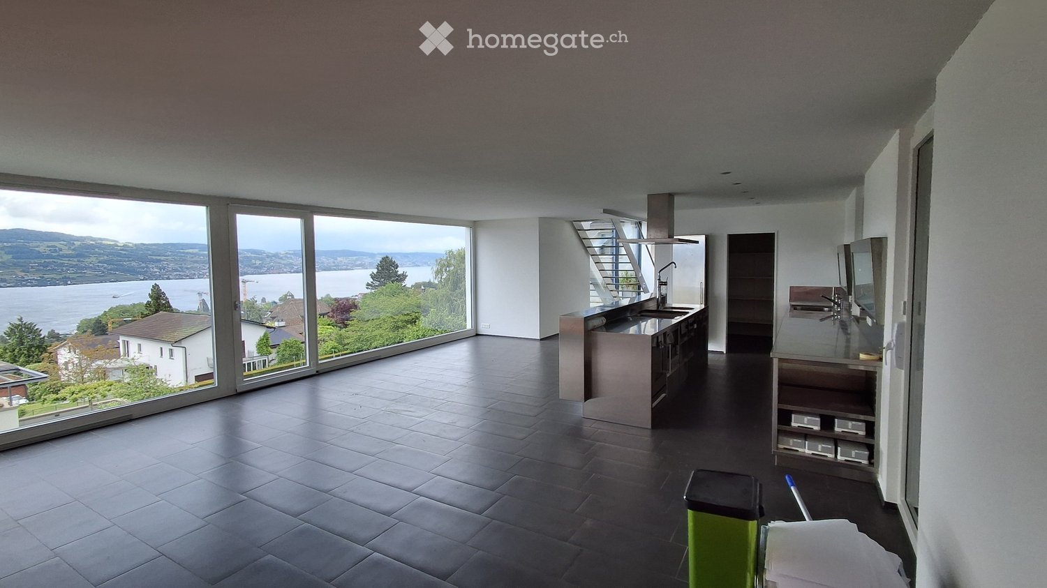 Kitchen. Modern kitchen with large windows offering a scenic view of a lake and surrounding landscape. Features include a stainless steel sink, faucet, stove, and built-in cabinets.