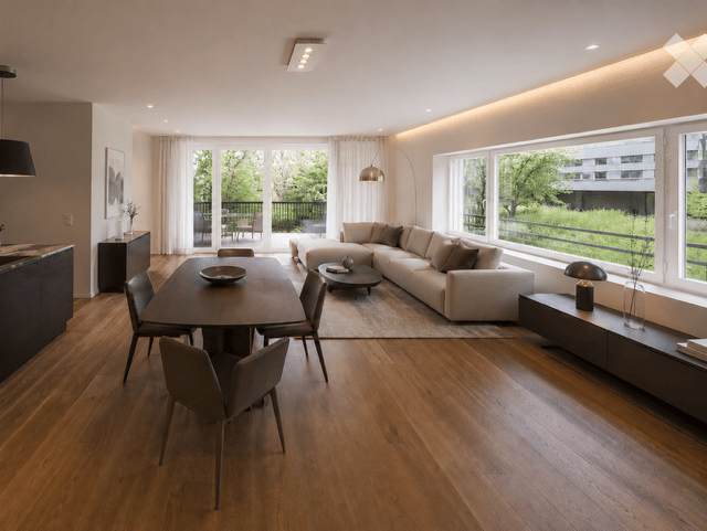Furnished Room. Modern open-plan living and dining area with hardwood flooring, large windows offering a view of greenery, a sectional sofa, coffee table, dining table with chairs, side table, and decorative items.