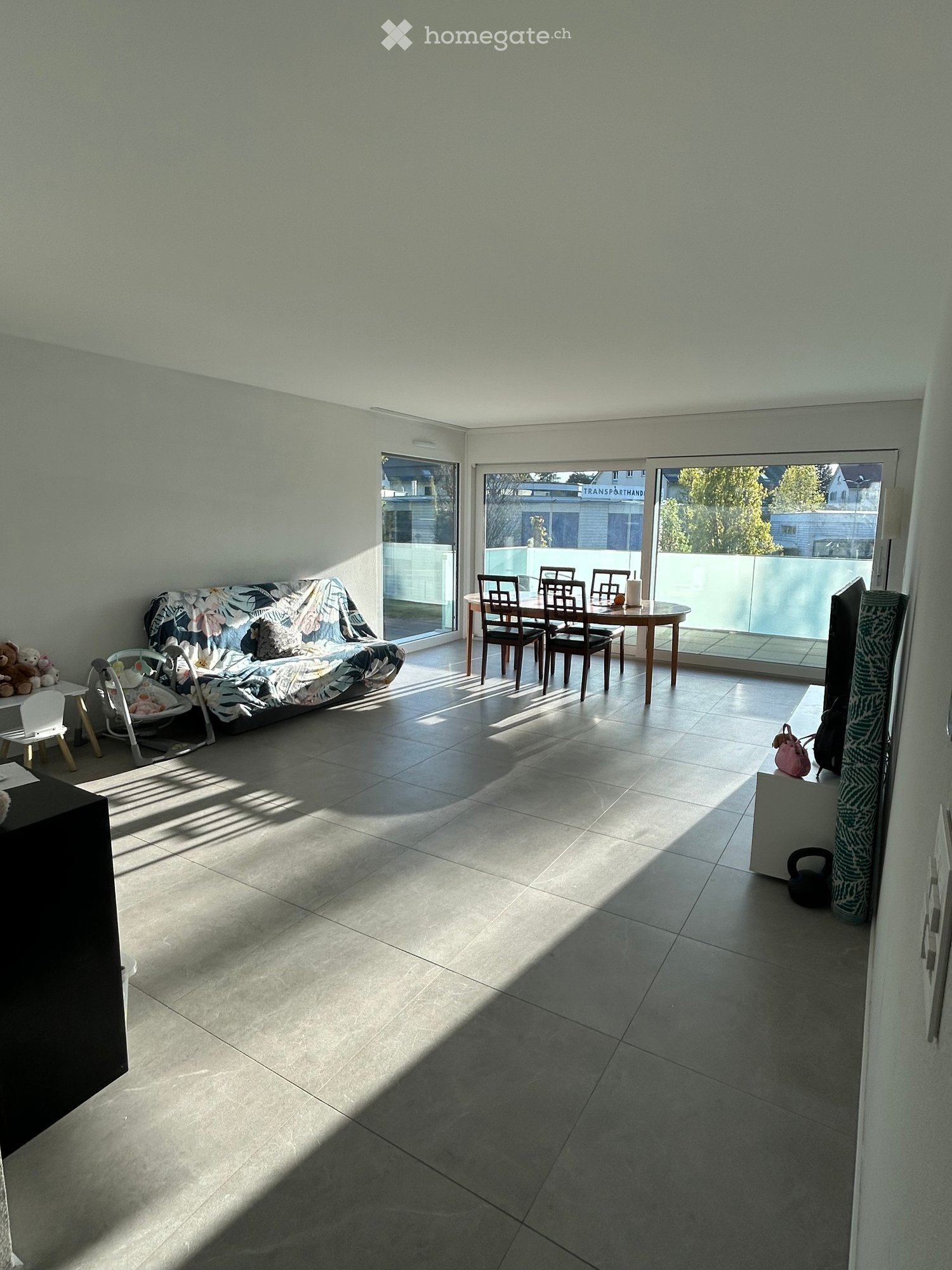Furnished Room. Bright living room with tiled floor, large windows, sofa, dining table, chairs, baby chair, and small stool.