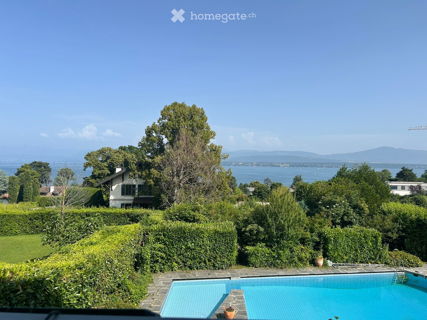 Garden / Outdoor Area. A serene garden area with a swimming pool, lush greenery, and a scenic view of a lake and distant mountains.