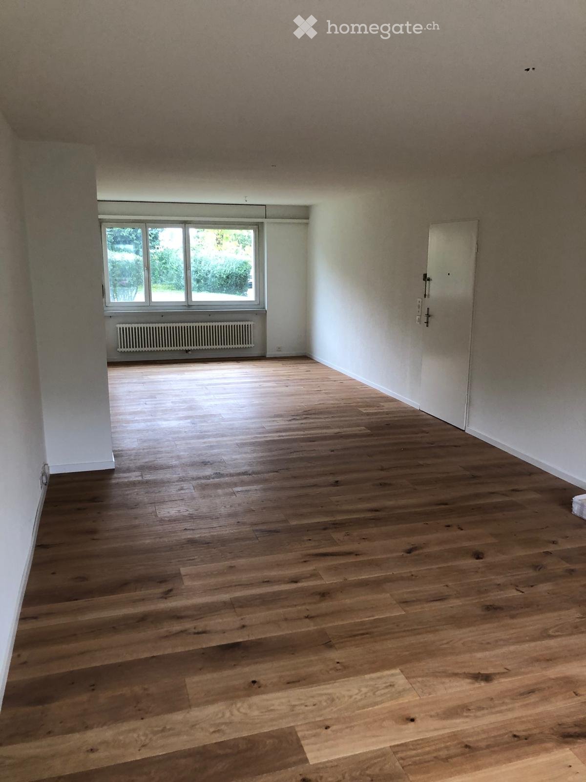 Unfurnished Room. Empty room with wooden flooring, white walls, and a large window with a radiator below it.