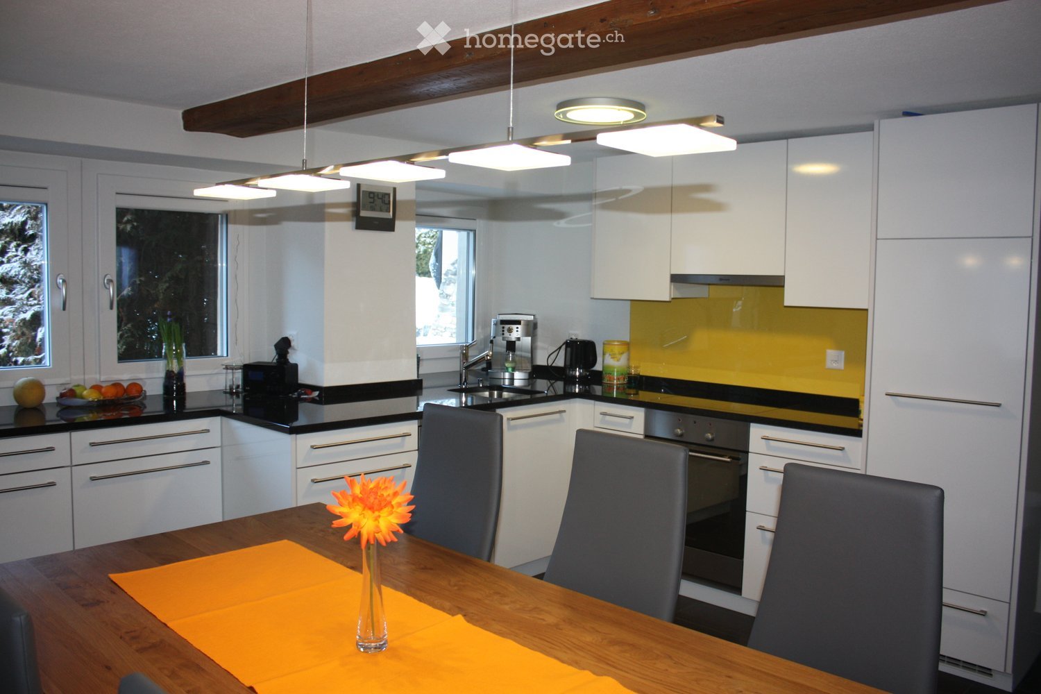 modern kitchen with dining area, white cabinets, yellow countertop, black countertops, table with flower, wooden chairs