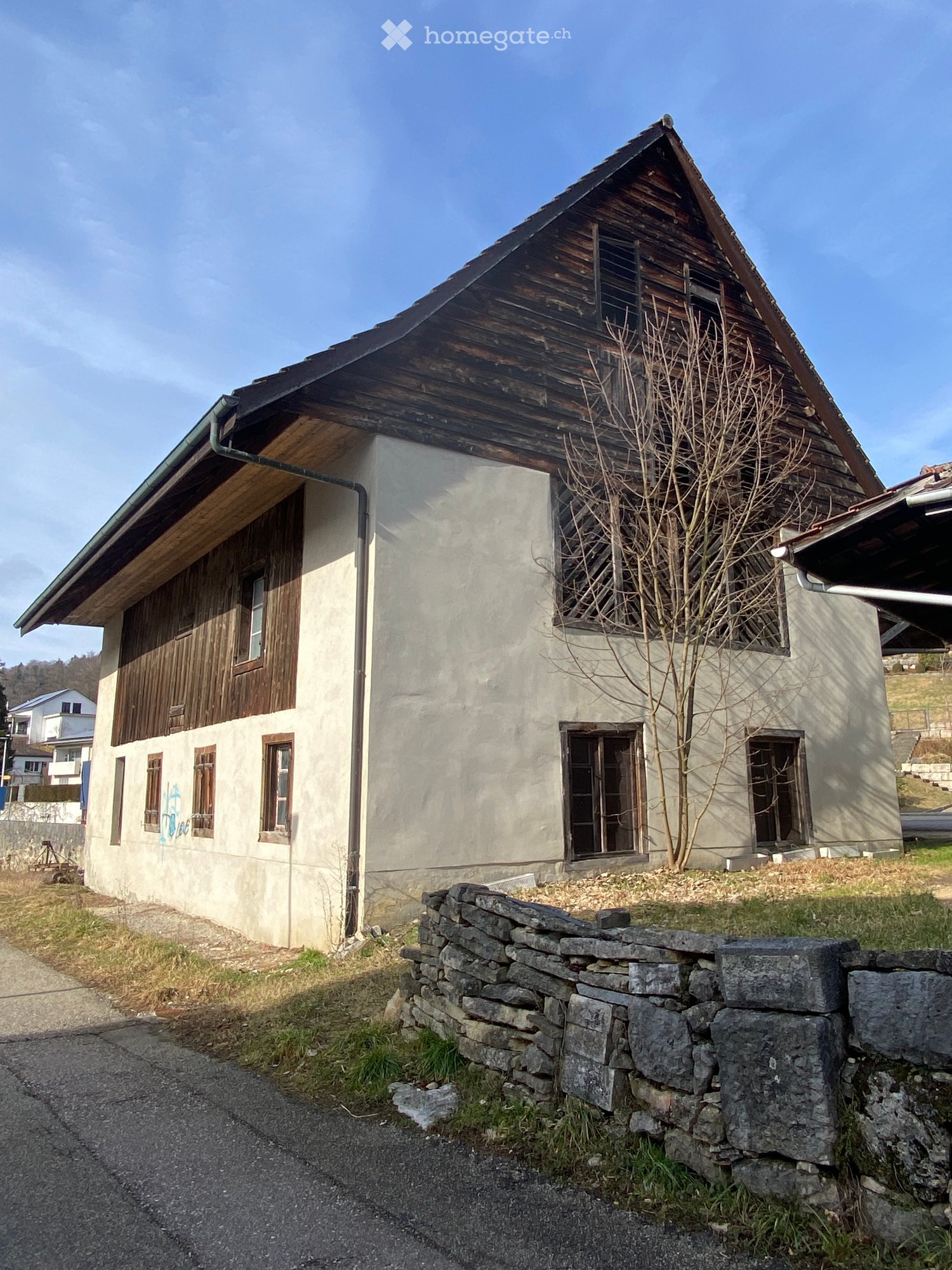 House. Two-story house with a wooden roof and stone walls, featuring multiple windows and a small tree in front.