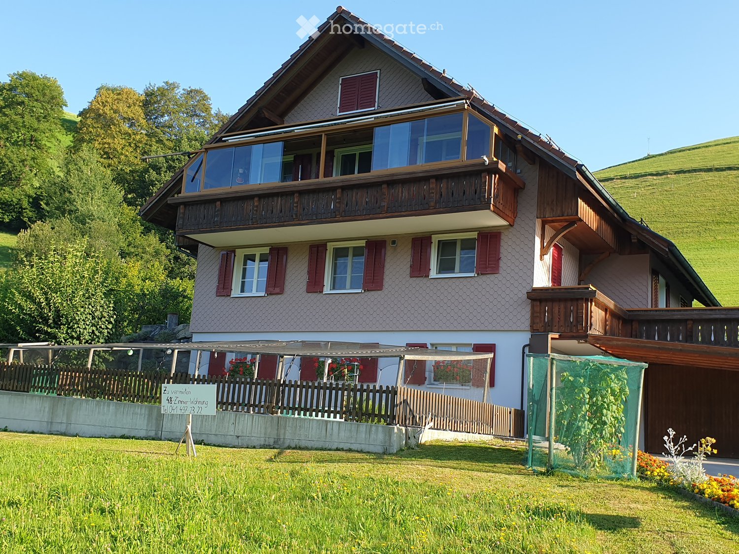 House. Two-story house with a balcony, red shutters, and a garden with a fence and plants.
