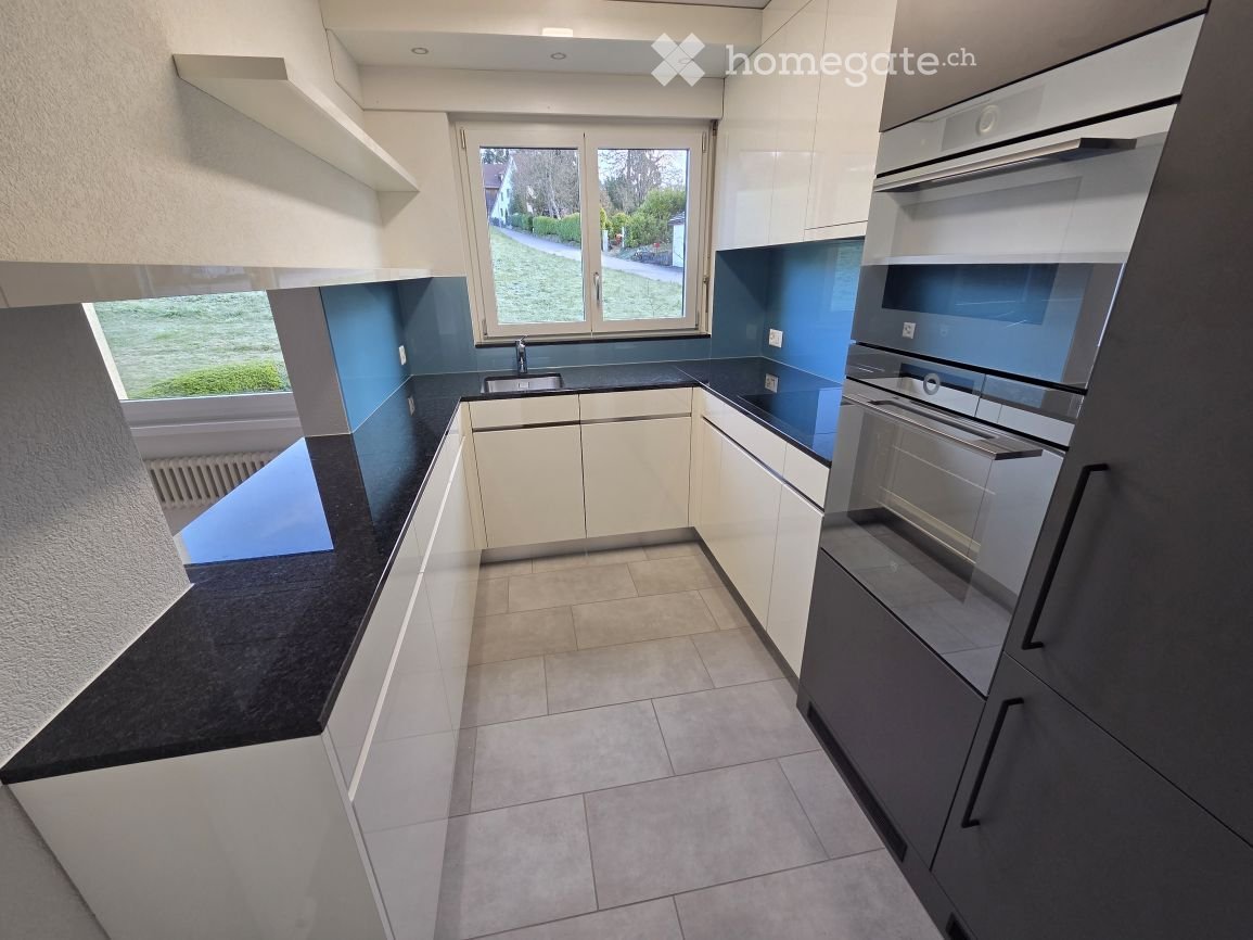 modern kitchen with white cabinets, black countertops, stainless steel appliances, large window