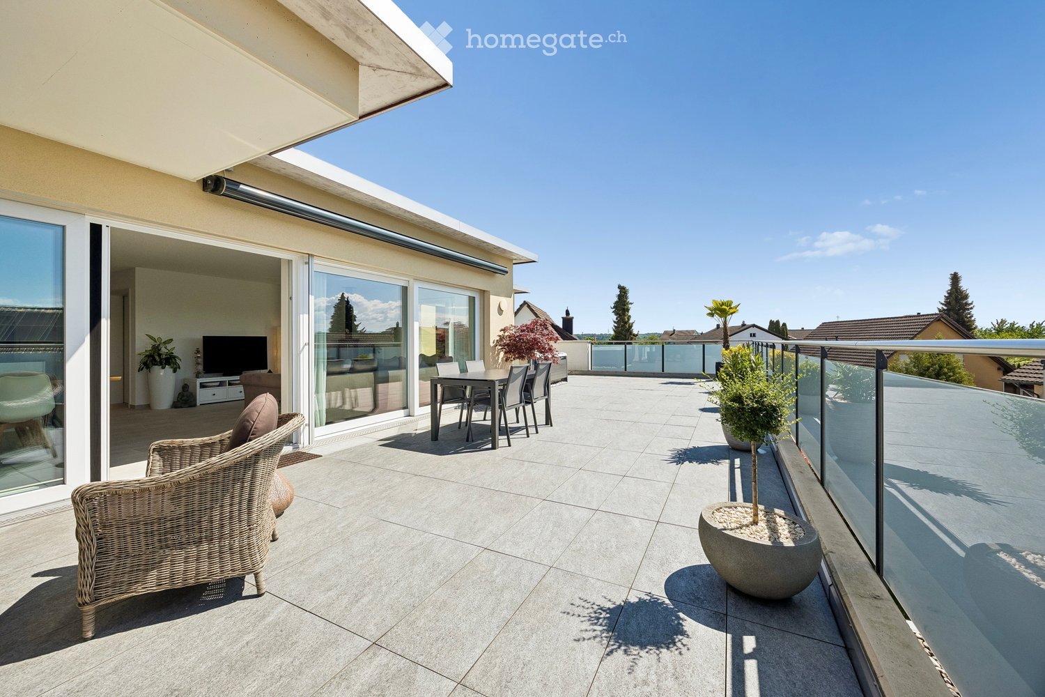 Balcony / Terrace. A modern rooftop terrace with a tiled floor, glass railing, and outdoor furniture including a wicker chair, dining table, and potted plants.